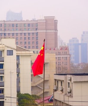 a red and yellow chinese flag in front of a city skyline